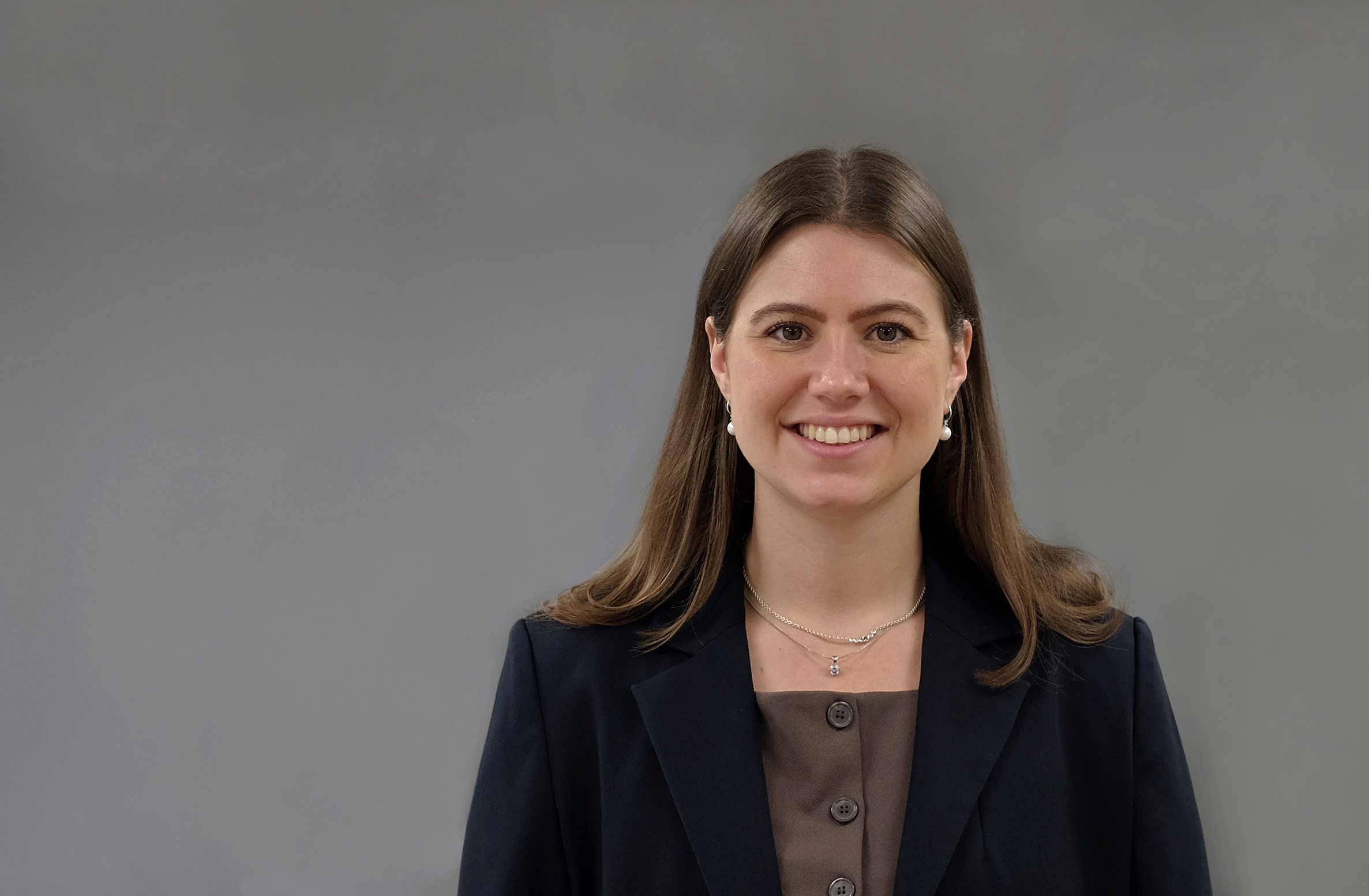 Lisa-Marie strahlt in die Kamera, trägt einen blauen Blazer und steht vor einem grauen Hintergrund